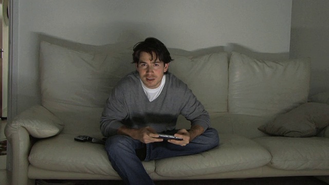 年轻男子坐在沙发上玩电子游戏/英国哈克尼视频下载