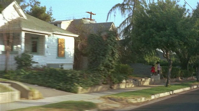 1955年，美国洛杉矶，两个孩子骑着自行车穿过绿树成荫的郊区街道视频素材