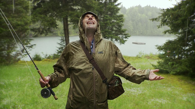 美国佛蒙特州莫里斯镇，一个微笑的男人拿着钓竿站在雨中，背景是湖视频素材