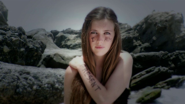 美国加州拉古纳海滩，十几岁的女孩站在岩石旁边，脸上写着“我”，手臂上写着“现在”视频素材