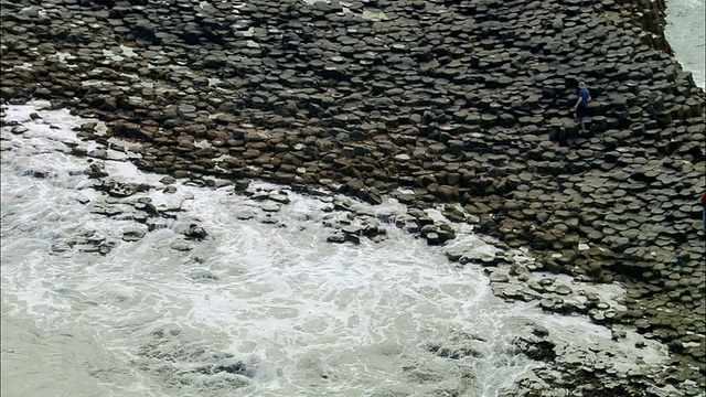 航拍宽镜头，在爱尔兰Coleraine涨潮时，两个人走在巨人的堤道上视频下载