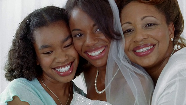 新娘、母亲和妹妹在相机前摆姿势/拍照/母亲和妹妹亲吻新娘的脸颊视频素材