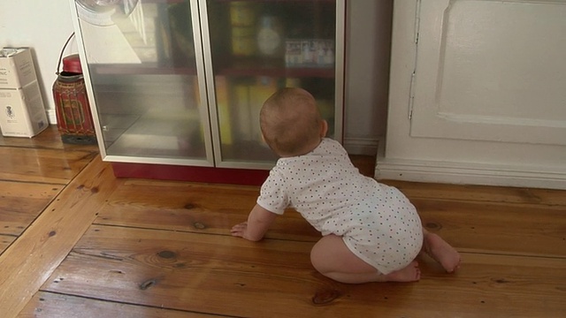 德国柏林，一个6-11个月大的女婴，爬向厨房橱柜，然后坐在那里看着摄像机视频素材