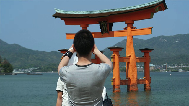 日本宫岛，涨潮时，严岛神社鸟居门前男子拍摄的夫妻合照视频素材