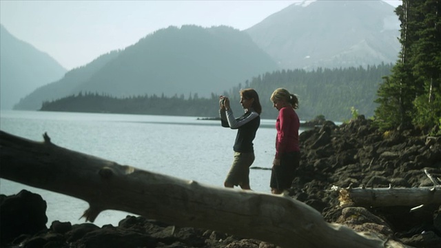 两名妇女站在湖边拍照，加里波第省公园，斯阔米什，加拿大不列颠哥伦比亚省视频下载