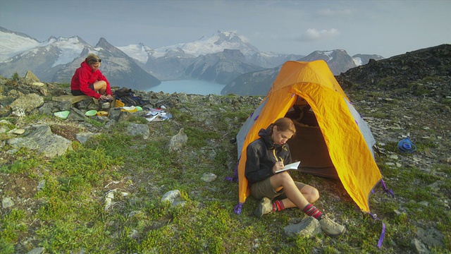 加拿大不列颠哥伦比亚省斯阔米什加里波第省公园的山顶上，两名女徒步者坐在她们的帐篷旁视频素材