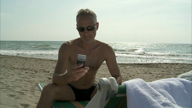 意大利罗马，一名坐在沙滩躺椅上玩手机的成熟男子视频下载