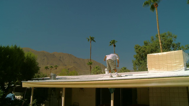 美国加州，在棕榈树环绕的沙漠中，一名油漆工在屋顶上工作。视频下载