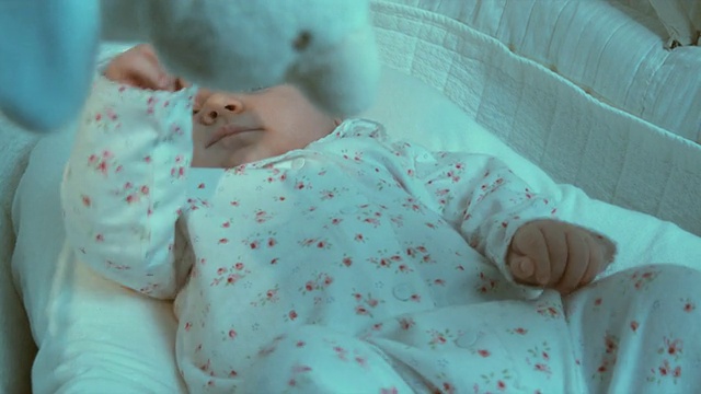 比利时布鲁塞尔，小女孩(2-5个月)躺在摩西篮子里，看着玩具在她的头上转动视频素材