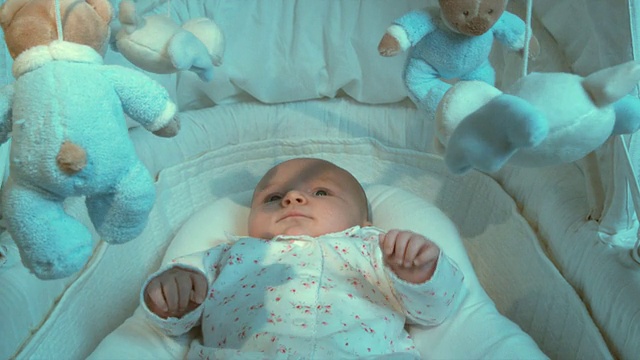 比利时布鲁塞尔，一个2-5个月大的女婴躺在摩西篮子里，看着玩具在她的头上转动视频素材
