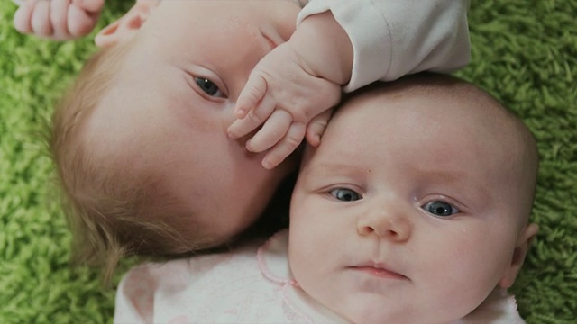 两名婴儿(2-5个月)躺在绿色地毯上的肖像，比利时布鲁塞尔视频素材