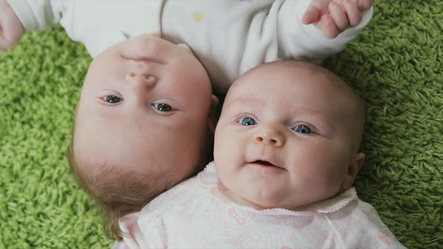两名婴儿(2-5个月)躺在绿色地毯上的肖像，比利时布鲁塞尔视频素材