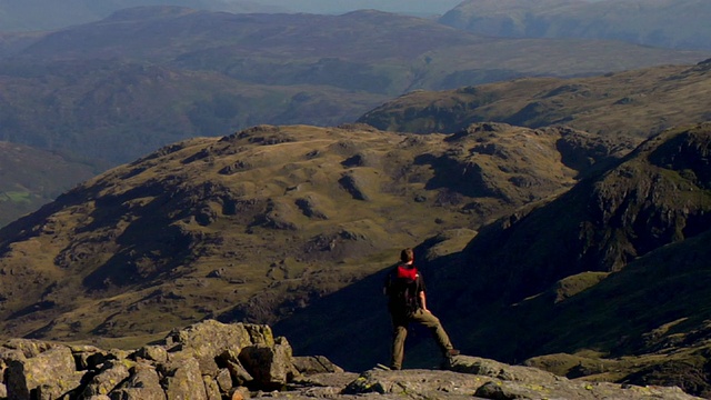 英国坎布里亚郡，一名年轻人从山上走下来，停下来欣赏山景视频素材