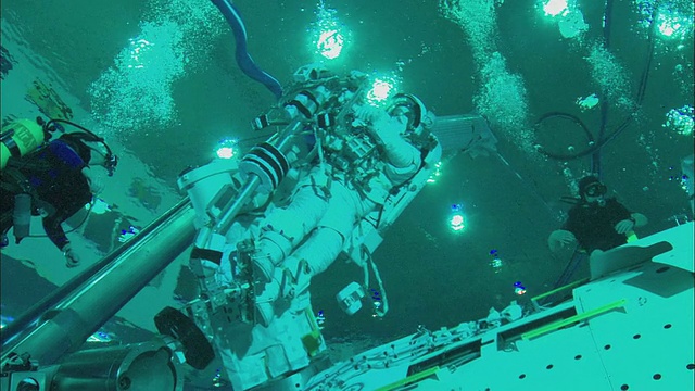 宇航员站在支撑臂上，在美国德克萨斯州休斯顿的中性浮力实验室的国际空间站模型一侧工作视频素材
