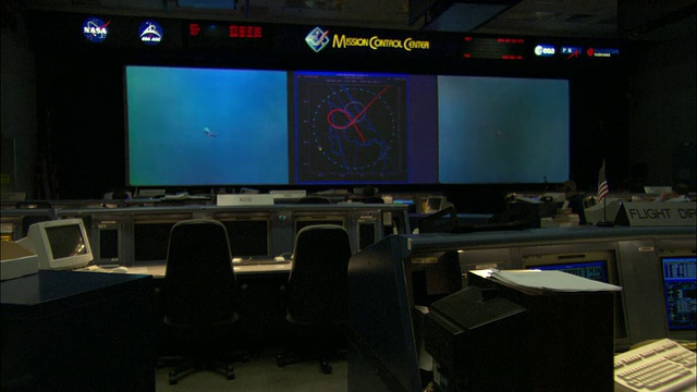 美国德克萨斯州休斯顿，任务控制室的空桌子上有电脑屏幕，主屏幕上显示x-38飞行器的测试下落视频视频素材