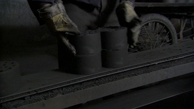 中国北京，一名工人正在将炭砖从传送带上运到他的三轮自行车的平板上视频下载