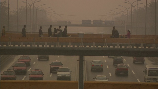 中国北京，早晨的高速公路交通在雾霾中，行人和骑自行车的人在天桥上经过视频下载