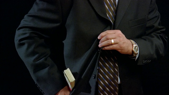 中等身材的男人把一捆捆的钱藏在西装外套里，然后扣上扣子视频下载
