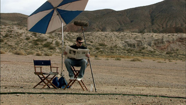 宽镜头变焦在boom操作员休息和阅读一份报纸沙漠电影设置/红石峡谷国家公园，加利福尼亚州视频下载