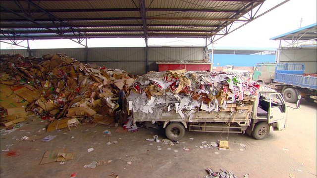 中国北京，在回收中心，两名工人正在清理卡车上覆盖着一大堆废纸的防水布视频素材