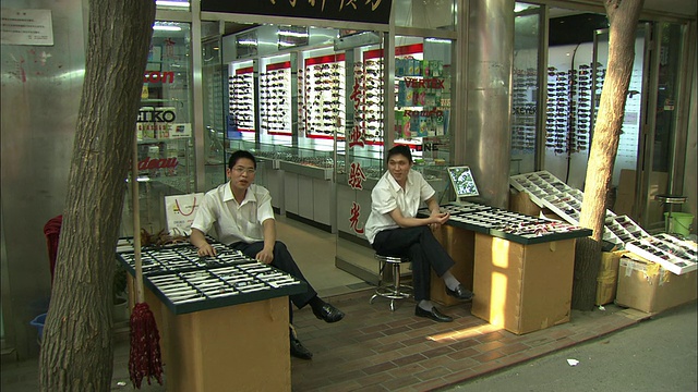中国，北京，北京，北京，北京光学城，两名戴眼镜的销售员坐在商店外的橱柜旁视频素材