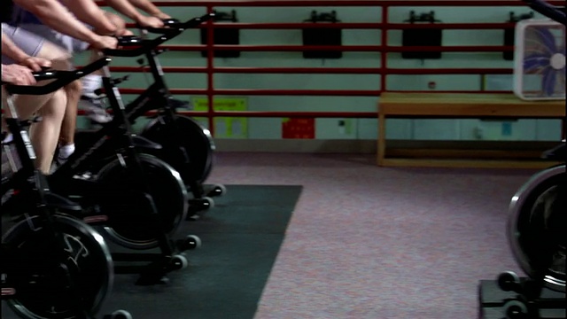 多莉拍摄了一排排的男人和女人在动感单车课上骑着固定自行车/教练在班上/近距离的脚踏板向后视频下载