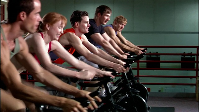 多利拍摄了一排排的男人和女人在动感单车课上骑固定自行车/站着和踩踏板视频素材
