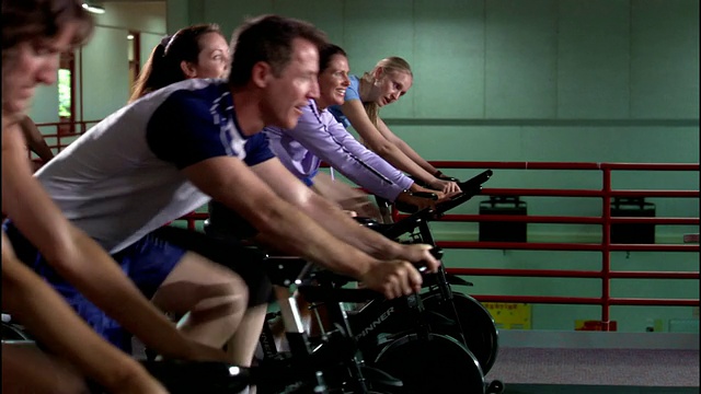 多莉拍摄了在动感单车课上一排排骑动感单车的男人和女人/站立和脚踏视频素材