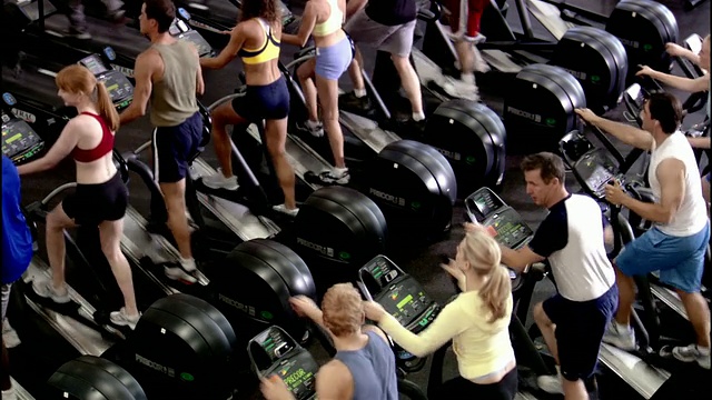 高角度广角拍摄男人和女人使用椭圆训练器在健身房视频素材