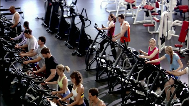 高角度广角拍摄男人和女人在健身房使用椭圆机和跑步机/男人使用pda视频下载