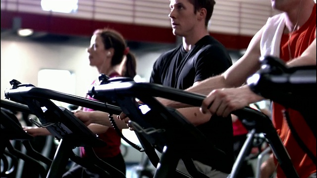 男人和女人在健身房使用椭圆训练机进行中长距离射击视频素材