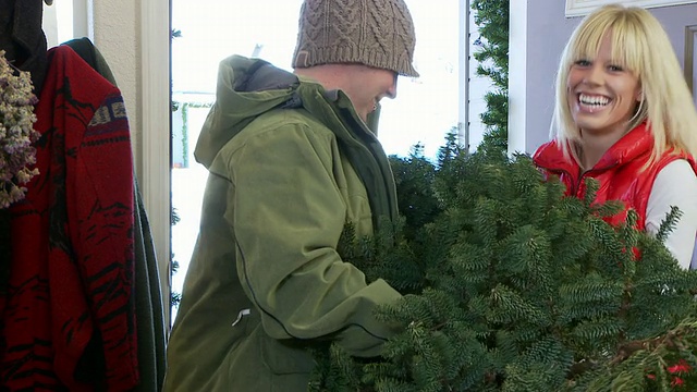 美国爱达荷州贝尔维尤，穿着冬装把圣诞树从前门带进来的夫妇视频下载