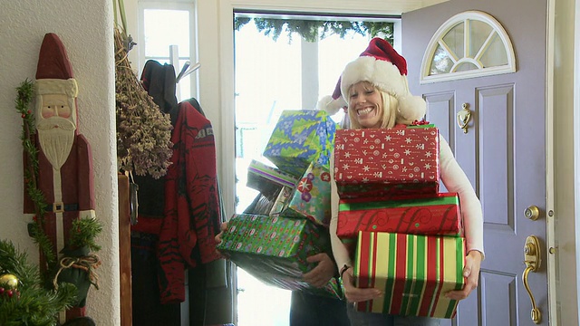戴着圣诞老人帽的夫妇从前门带来礼物和包装纸/美国爱达荷州贝尔维尤视频素材