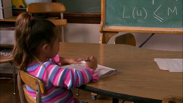 中等拍摄的年轻女孩坐在桌子上写字/倾斜女孩站在黑板上写满了数学方程视频素材