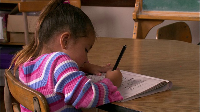 中等镜头的年轻女孩坐在桌子旁练习她的字母/倾斜女孩站在黑板上试图解决数学问题视频下载