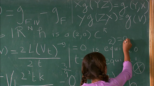 中镜头后视图的女孩在黑板上计算数学问题/转身，看起来很满意视频下载