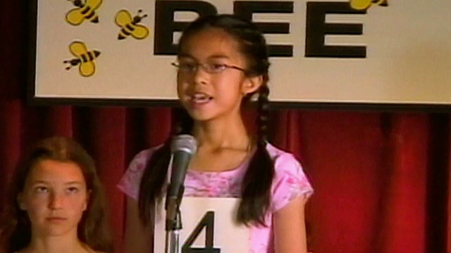 拼写比赛的主持人从讲台后面宣布单词/潘对着麦克风的女孩拼写单词/坐下来/洛杉矶，加利福尼亚视频素材