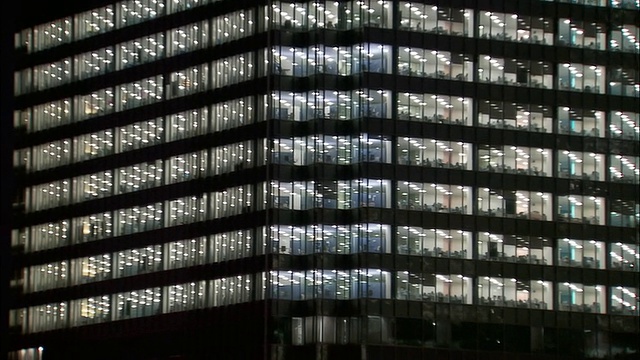 在晚上办公大楼的宽镜头窗户/放大中景与可见的人在/伦敦视频下载