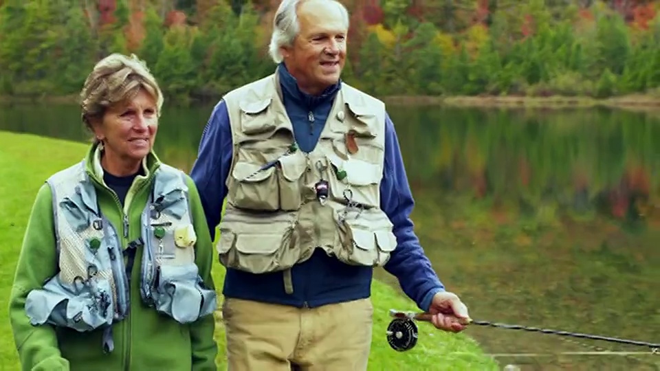 在美国佛蒙特州曼彻斯特，一对老年夫妇带着钓竿沿着湖岸散步，面带微笑，谈笑风生视频下载