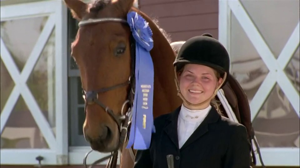 骑马比赛的获胜者与佩戴蓝丝带的马摆姿势的肖像视频素材