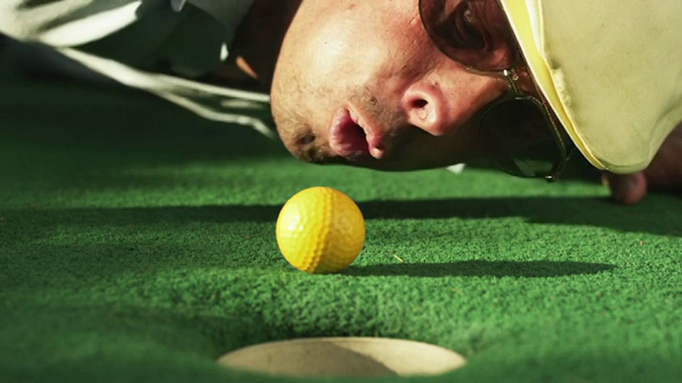 一名男子躺在高尔夫球场的果岭上，将高尔夫球吹向美国犹他州奥勒姆洞视频下载