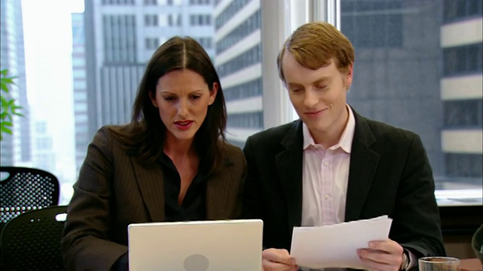 中等镜头的男人和女人看着笔记本电脑，在会议室里交谈，纽约视频素材