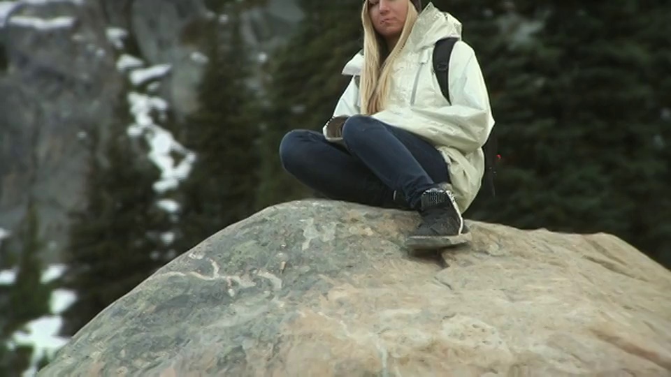 年轻女子坐在岩石上，背景是惠斯勒山/加拿大不列颠哥伦比亚省惠斯勒视频下载