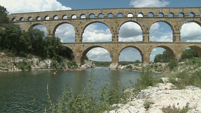 法国朗格多克-鲁西永，加德河的WS Pont du Gard，罗马高架渠，人们在远处的加德河上划独木舟视频下载