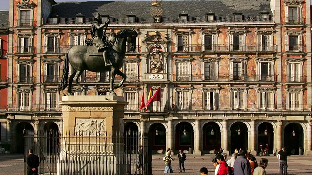 从Casa de la Panaderia外部的盾形纹章中缩小镜头，可以看到行人在市长广场的费利佩三世雕像前的快速移动/西班牙马德里视频素材