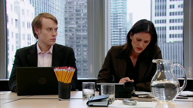 在办公室会议室里，中等镜头的男人以挑逗的方式盯着女人/女人转过身去看/男人往嘴里喷口气清新剂/纽约，纽约视频素材