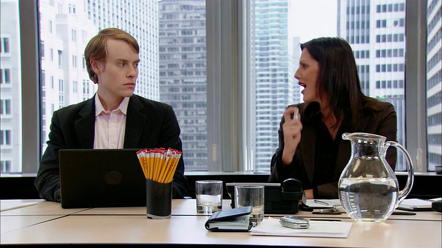 中镜头的男人和女人坐在办公室会议室的桌子旁/一个男人回头看到一个女人盯着他/一个女人往嘴里喷呼吸喷雾并对着他微笑/纽约，纽约视频素材