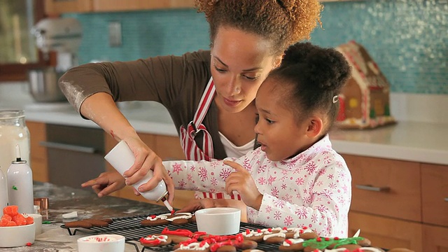 美国弗吉尼亚州里士满，母亲和女儿(4-5岁)在厨房里装饰姜饼视频素材