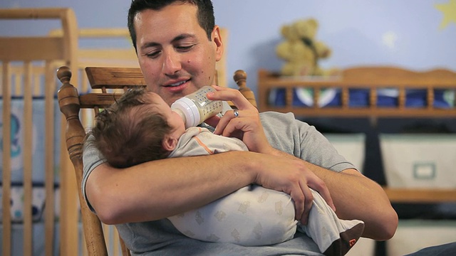 美国弗吉尼亚州里士满，父亲在婴儿室用奶瓶给2-5个月大的男婴喂奶。视频素材