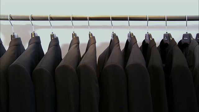 比利时布鲁塞尔，一名男子的手推着挂在衣架上的一排黑色夹克视频下载